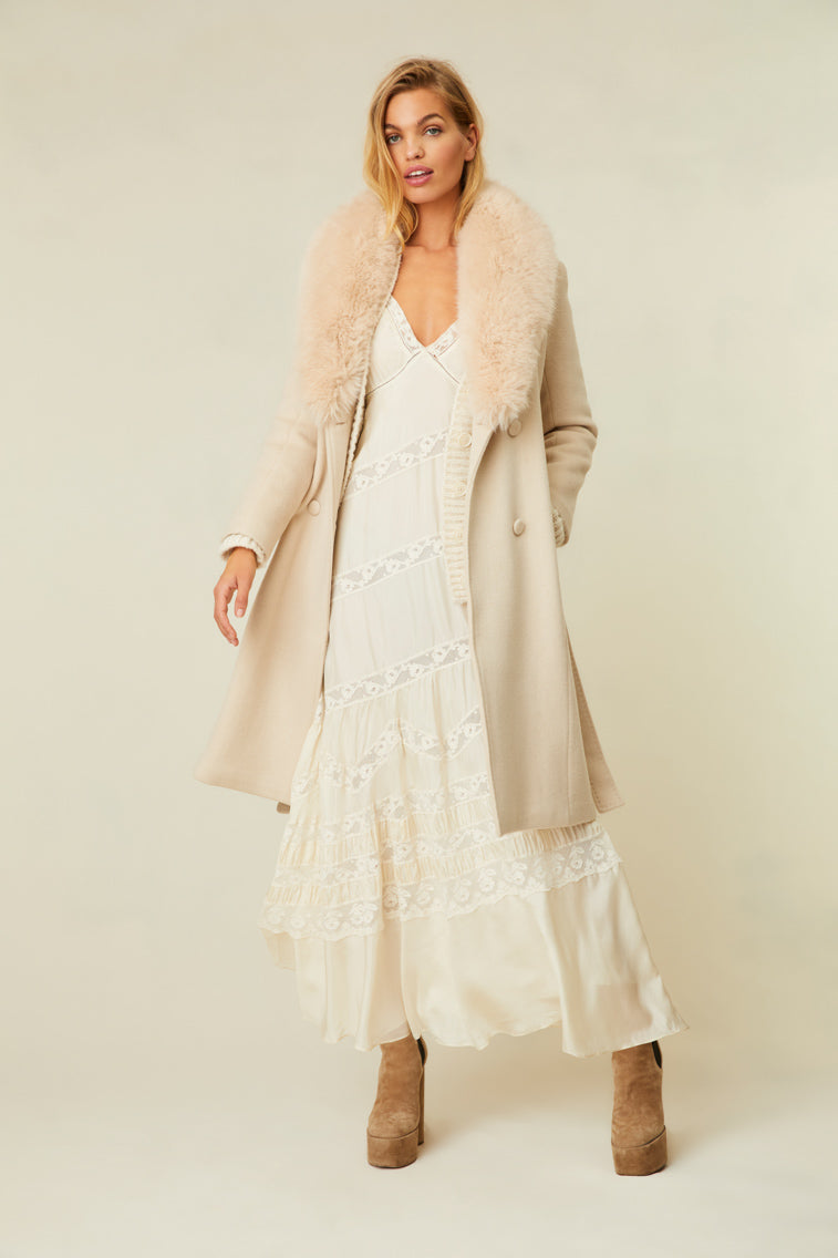 The cream-colored jacket features a faux fur collar, pockets, and a belt.