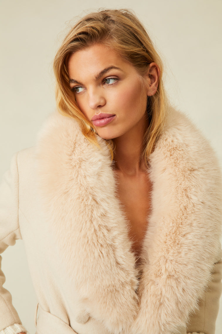 The cream-colored jacket features a faux fur collar, pockets, and a belt.