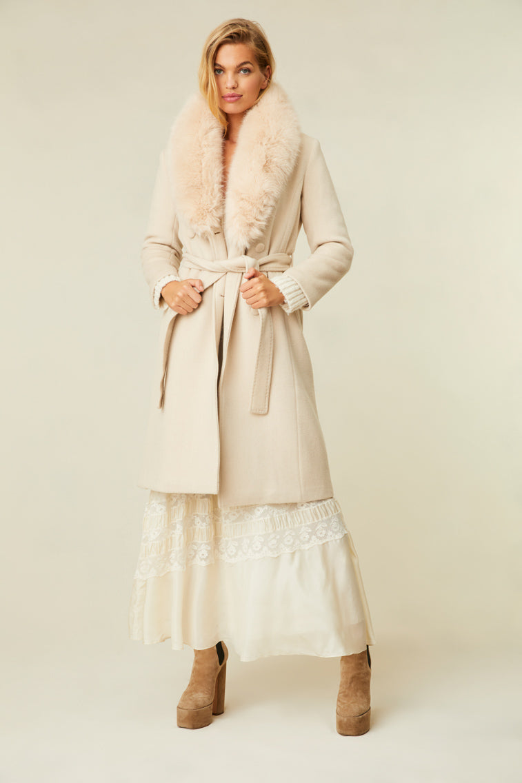 The cream-colored jacket features a faux fur collar, pockets, and a belt.