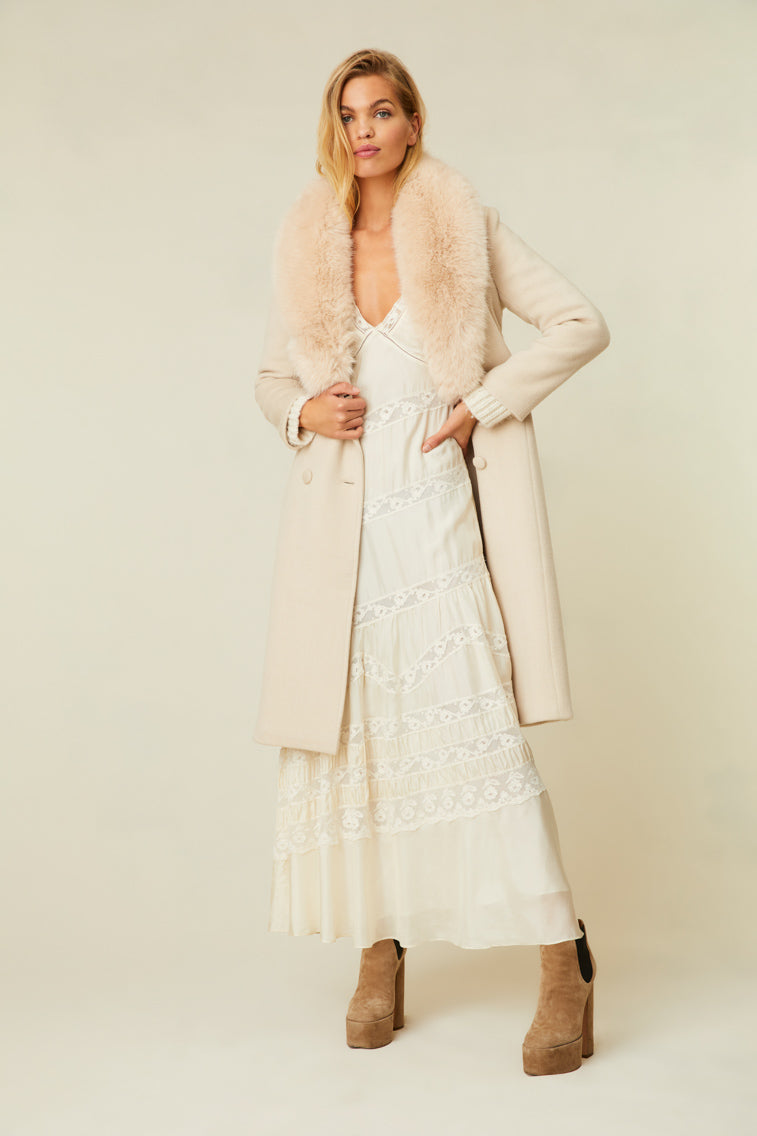 The cream-colored jacket features a faux fur collar, pockets, and a belt.