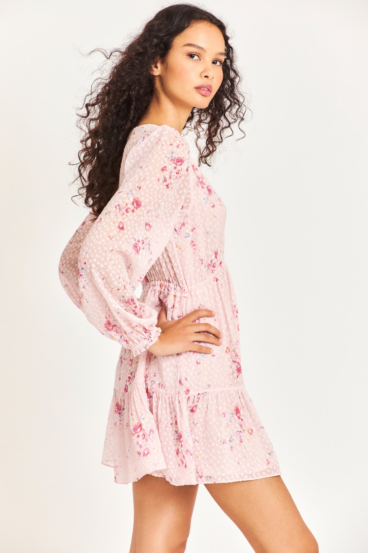 Side image of model wearing pink mini dress with flower detail