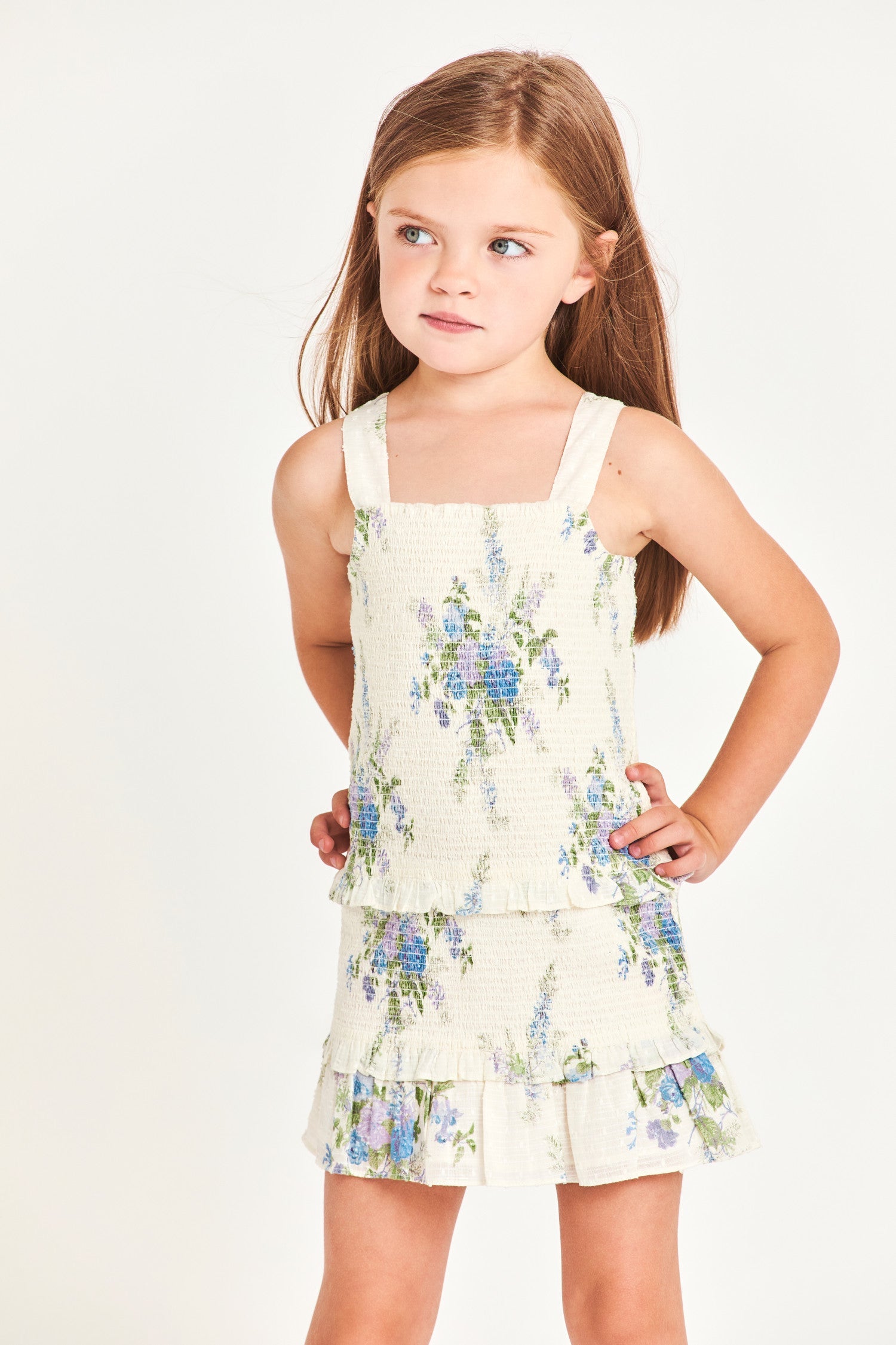 The girl’s Clancey dress is a white 100% cotton dress with blue flower detailing. It features a ruffled two-tier bottom and waistband. 