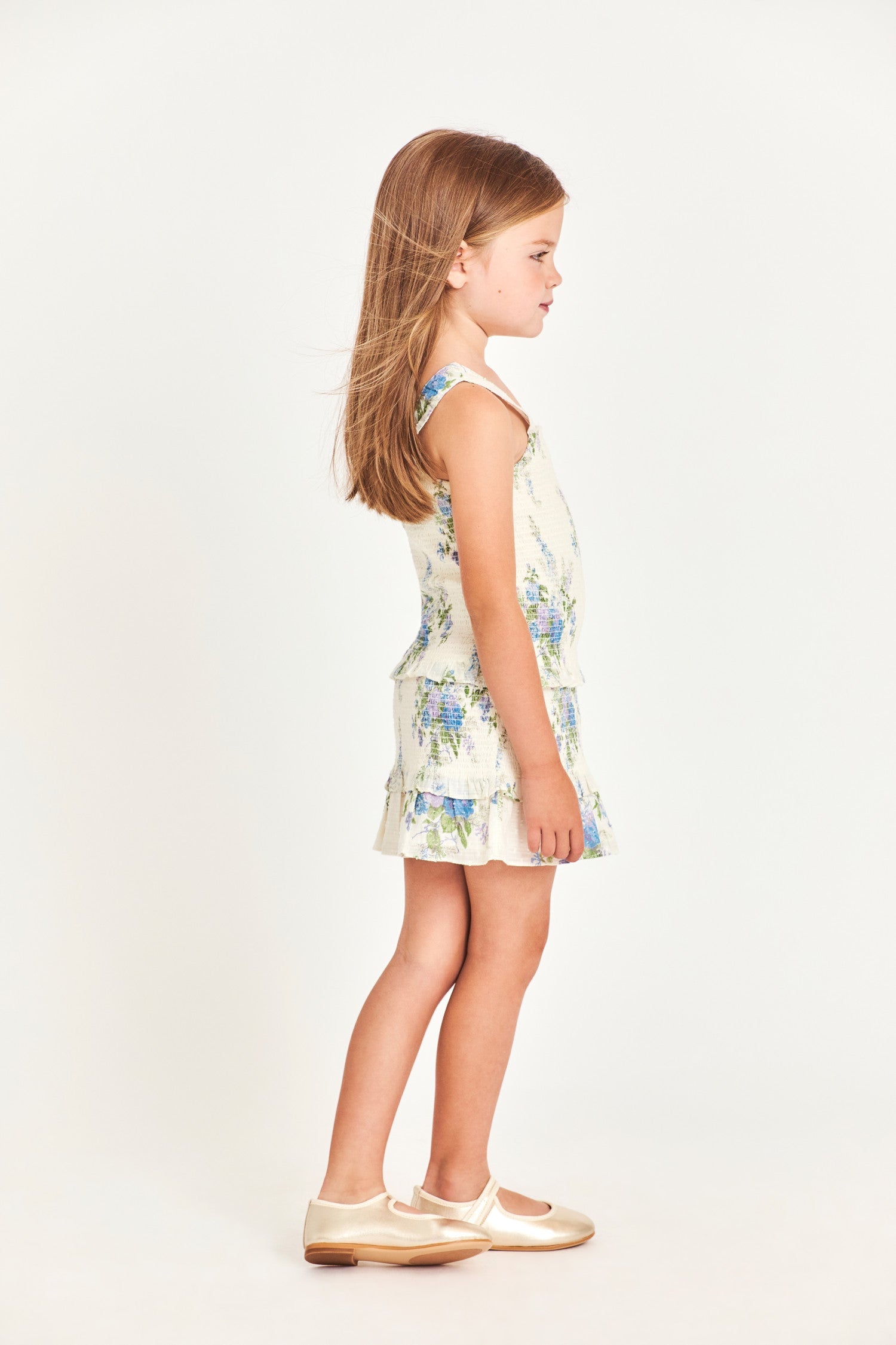 The girl’s Clancey dress is a white 100% cotton dress with blue flower detailing. It features a ruffled two-tier bottom and waistband. 