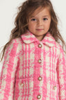 Little girl with pink and white houndstooth print wool jacket with pearl buttons, and pockets.