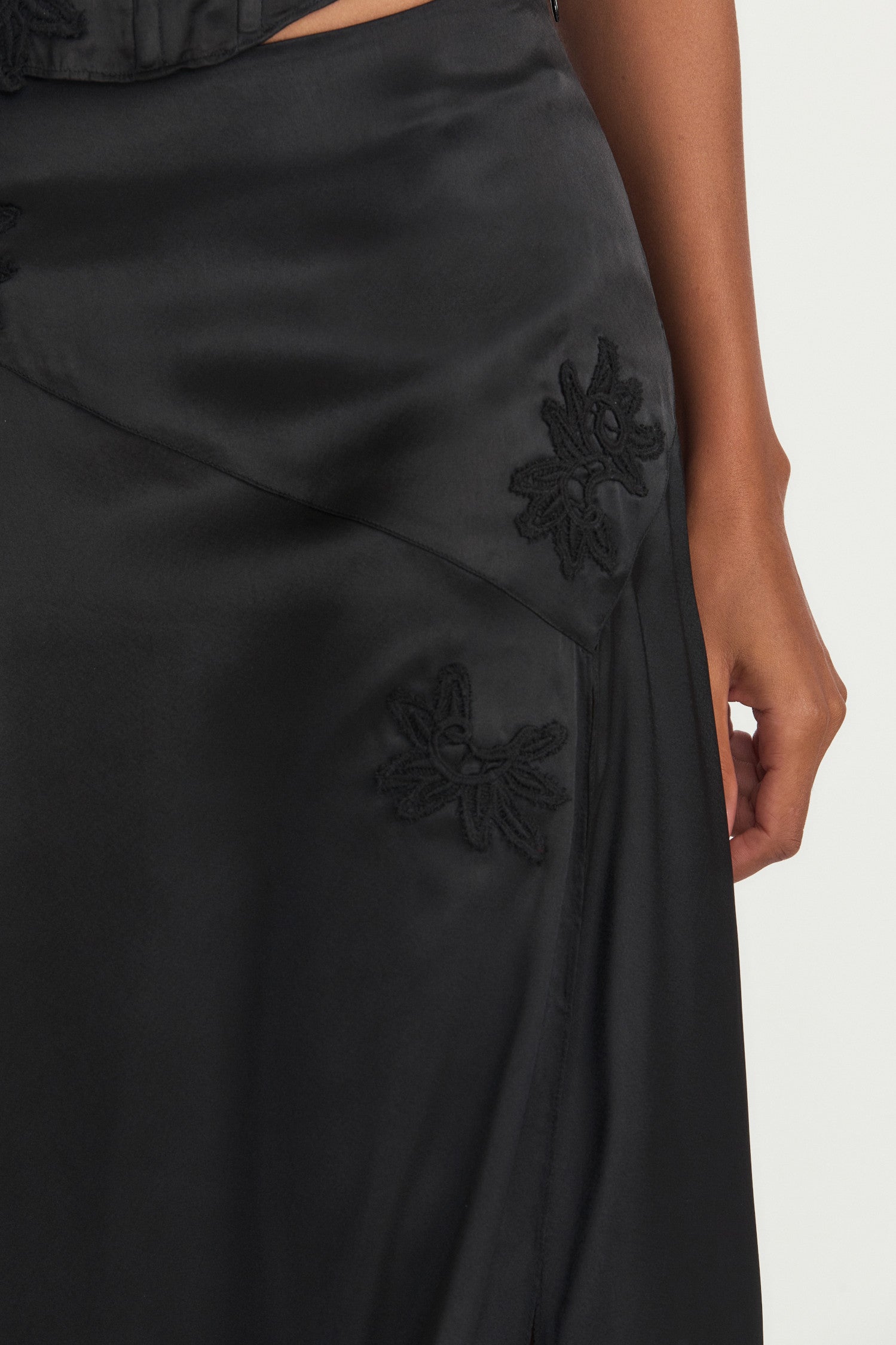 Black silk long skirt with lace motif douses around the yolk and a fixed waist above an off-center, enlarged, zigzag seam detail. Below, the piece flows to the ankle with a slit on the wearer’s left.