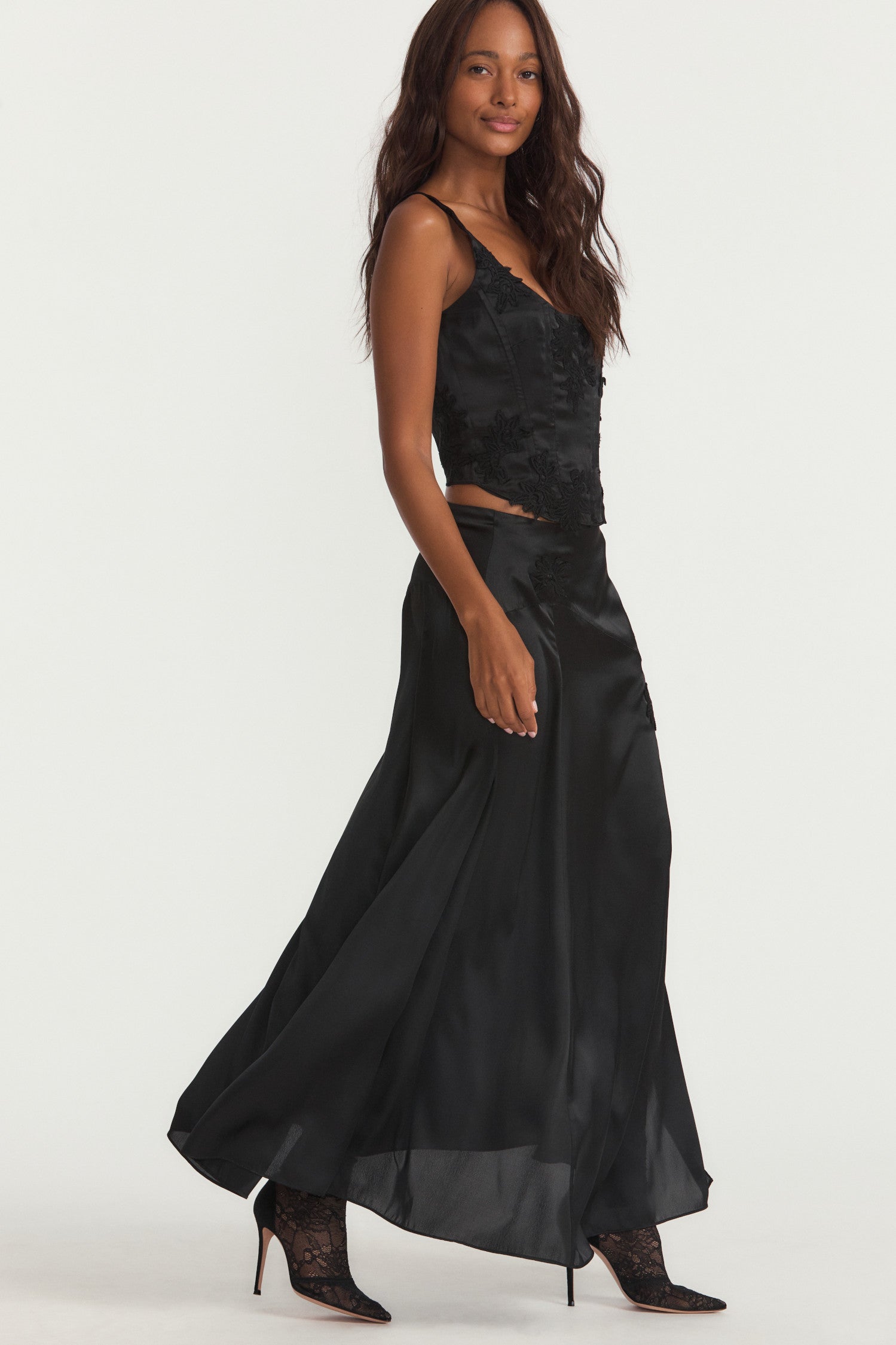 Black silk long skirt with lace motif douses around the yolk and a fixed waist above an off-center, enlarged, zigzag seam detail. Below, the piece flows to the ankle with a slit on the wearer’s left.