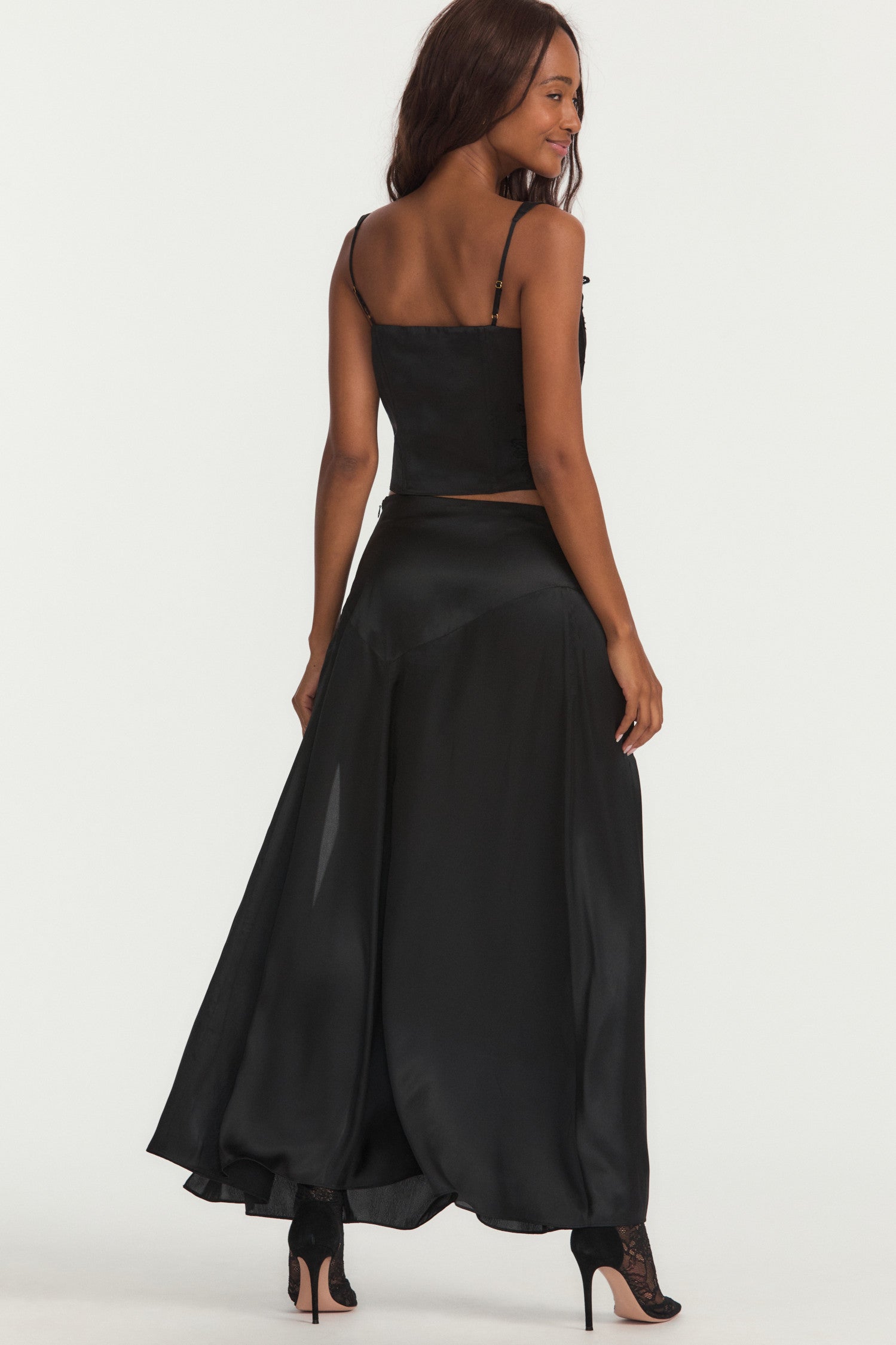 Black silk long skirt with lace motif douses around the yolk and a fixed waist above an off-center, enlarged, zigzag seam detail. Below, the piece flows to the ankle with a slit on the wearer’s left.