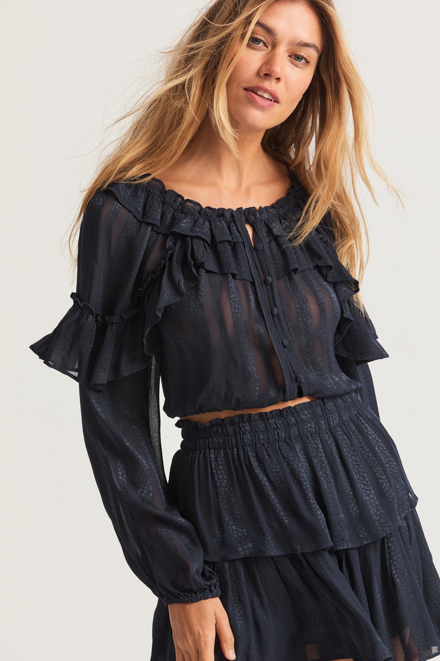 Black long sleeved-top features a striped jacquard fabric, dramatic ruffles all over, an elasticated waist, elastic at the sleeve openings, and a fully functioning center front slit.