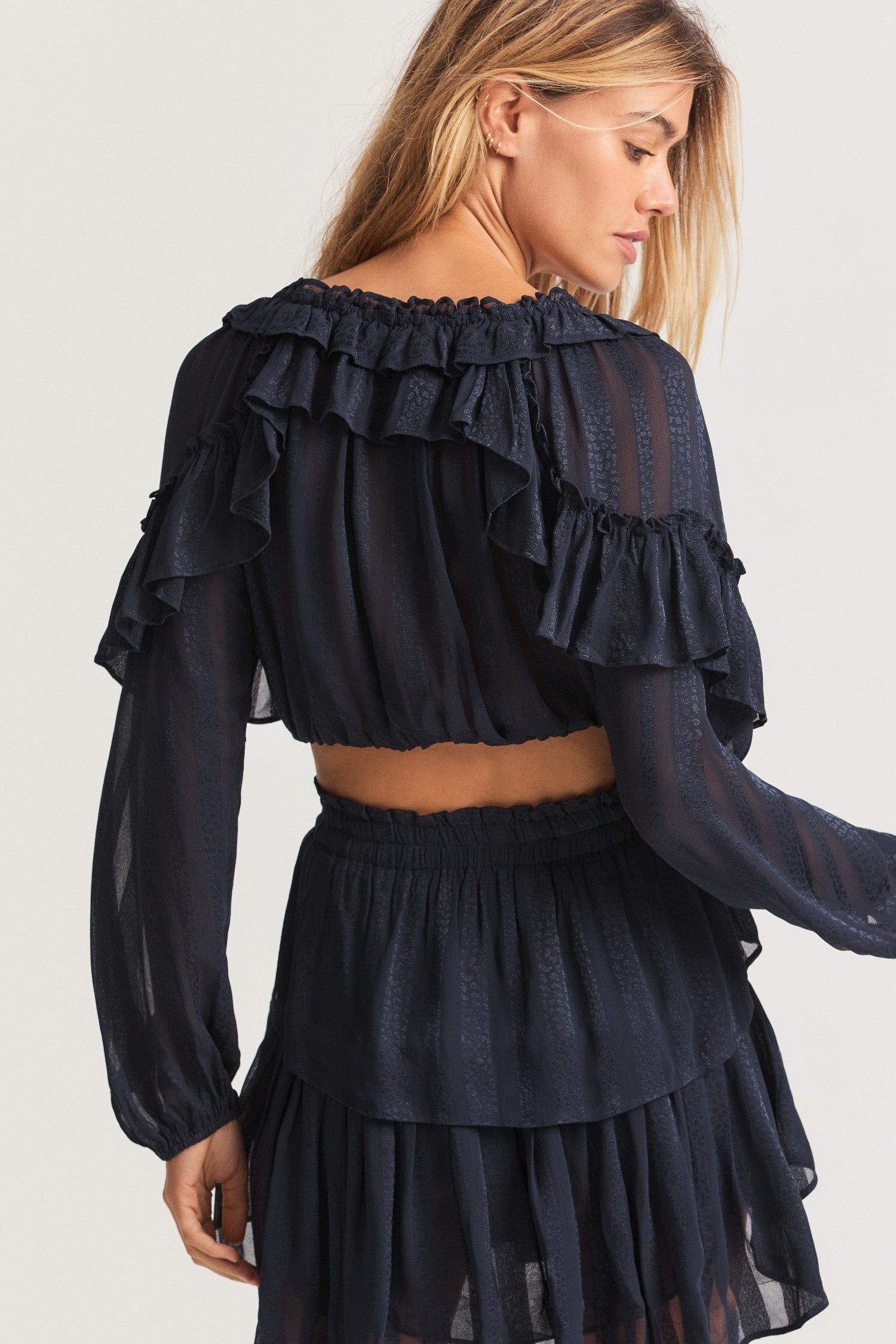 Black long sleeved-top features a striped jacquard fabric, dramatic ruffles all over, an elasticated waist, elastic at the sleeve openings, and a fully functioning center front slit.