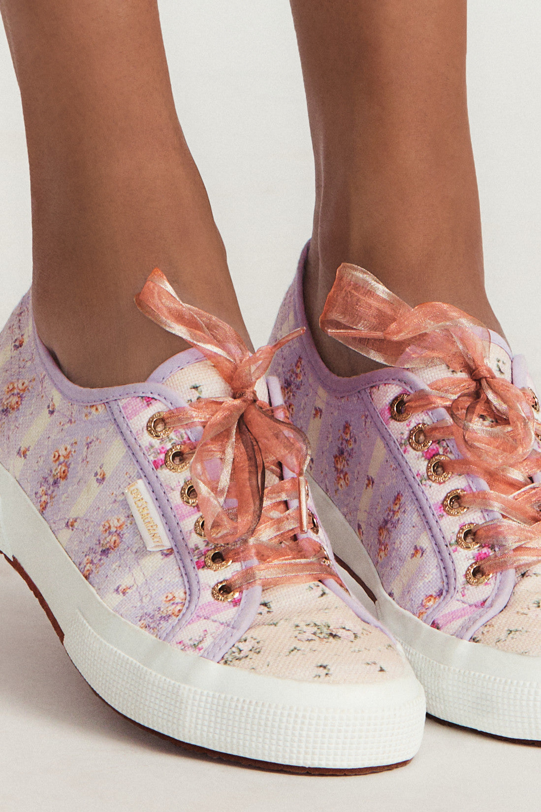 Pastel lilac sneaker with floral pattern on printed cotton, gold-toned eyelet details, and pink organza laces.