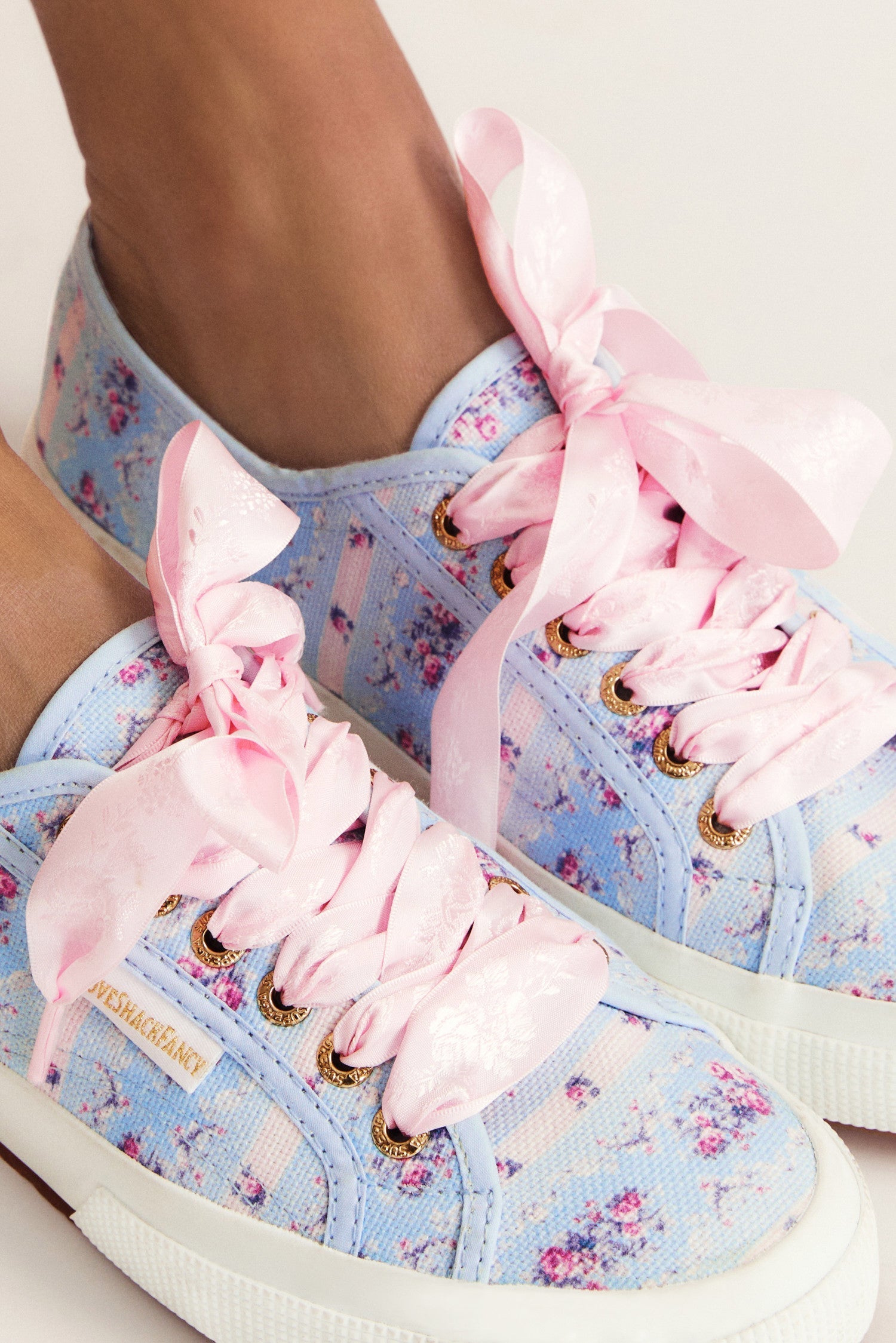 Pastel blue sneaker with floral pattern on printed cotton, gold-toned eyelet details, and pink velvet laces.