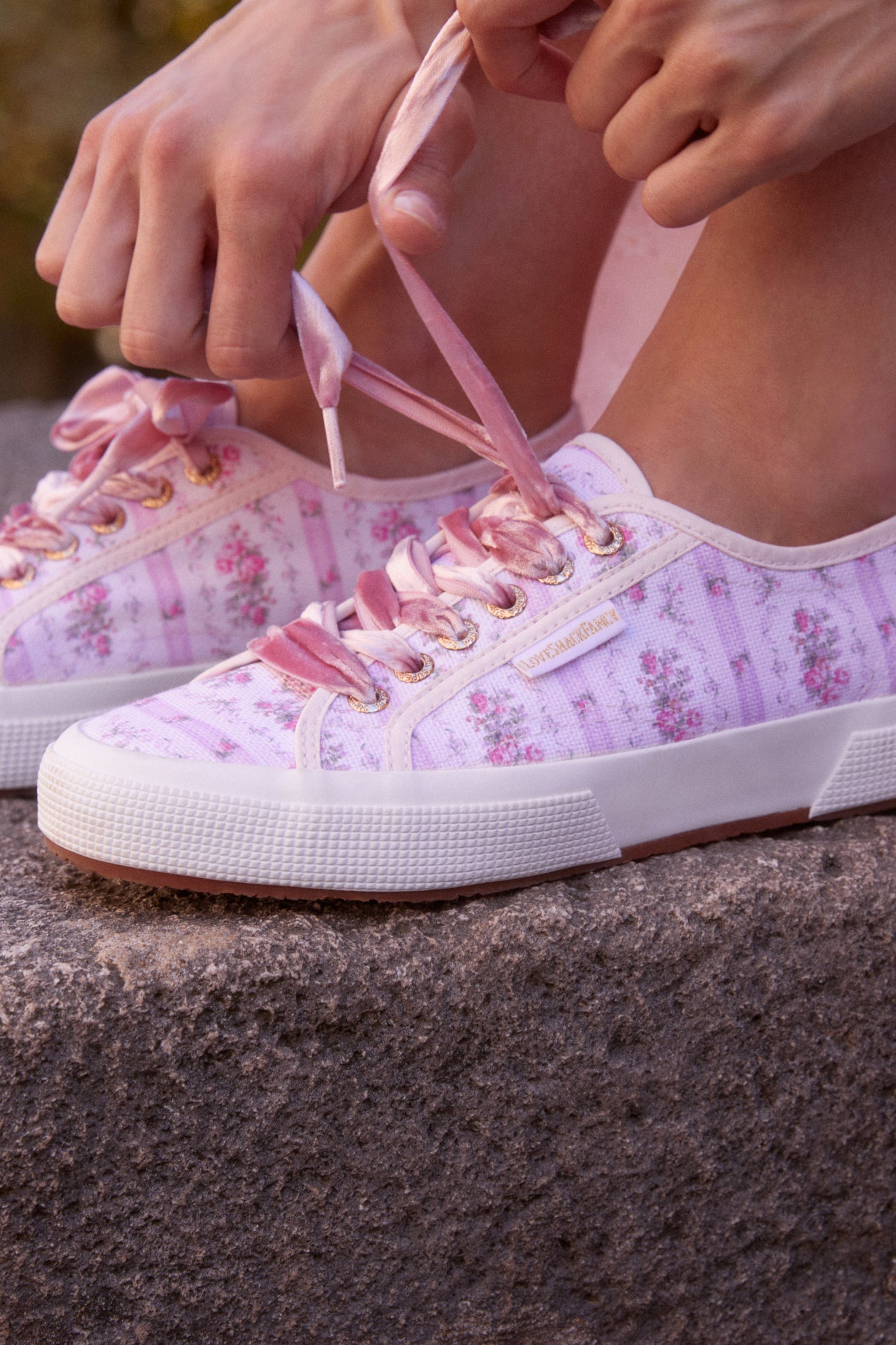 Pastel pink sneaker with floral pattern on printed cotton, gold-toned eyelet details, and pink velvet laces.