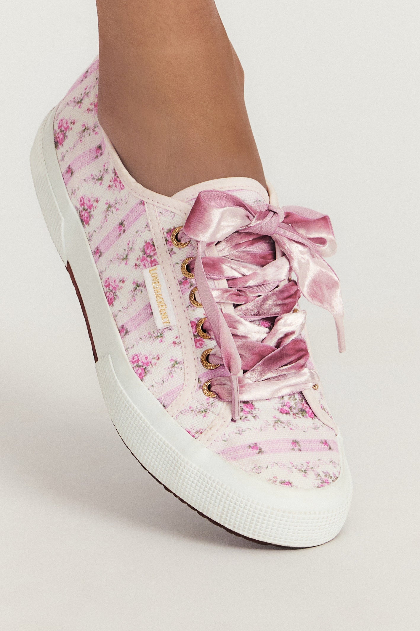 Pastel pink sneaker with floral pattern on printed cotton, gold-toned eyelet details, and pink velvet laces.